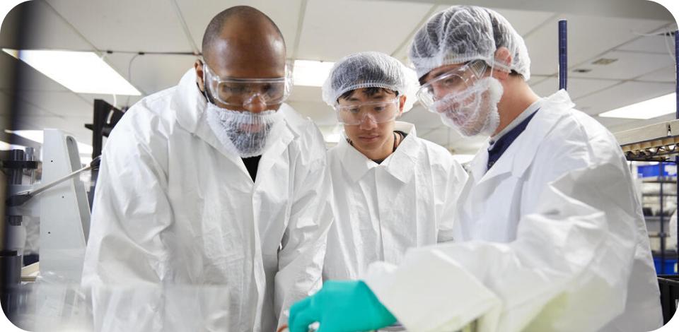 Trois personnes en tenue de laboratoire regardant une solution liquide.